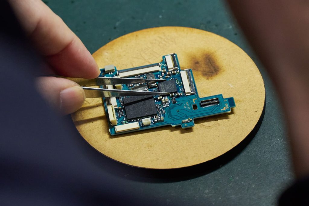 クロック用発振器がピンセットの下あたりに並ぶ銀色の四角。AFEがピンセットで挟んでいるもの。メインプロセッサはボード左下の大きな四角