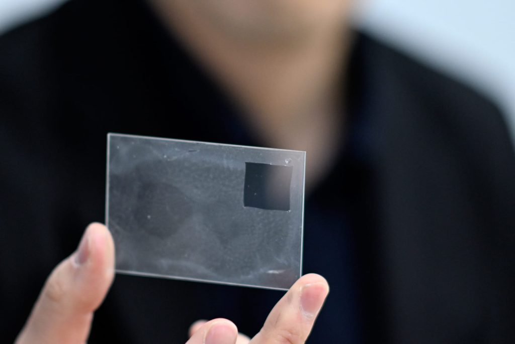 ガラス板に貼ってある状態の「見えない電極」（右上の四角い部分は切り取って使用した跡）。水に溶けるシート上につくってあり、水を含ませて皮膚に貼りつけるとシートが溶け、ほぼ目視できなくなる